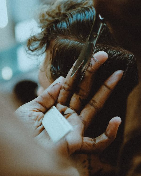 A mão do Higor segurando o pente e a tesoura no cabelo